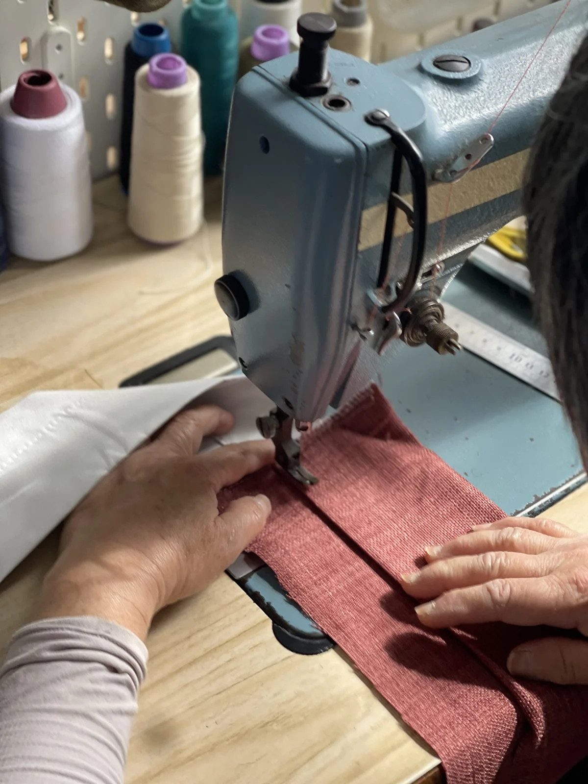 Hands guiding red fabric through a sewing machine in our studio